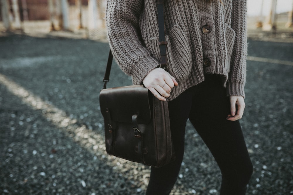woman in gray sweater and black pants holding black leather sling bag