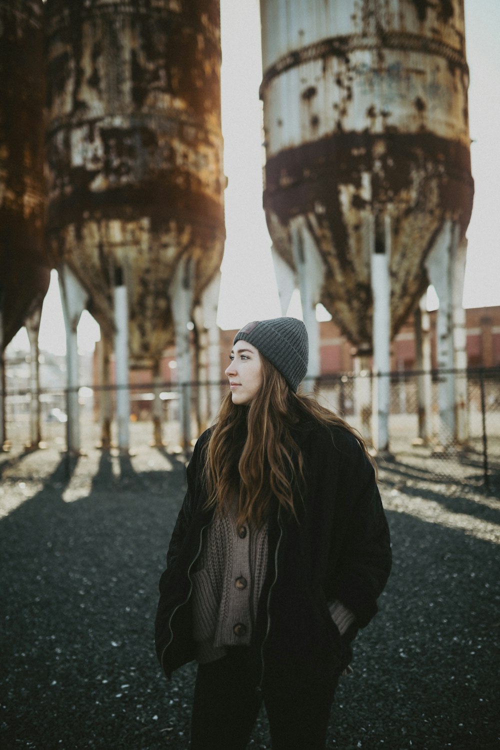 woman in black jacket and knit cap standing on road during daytime