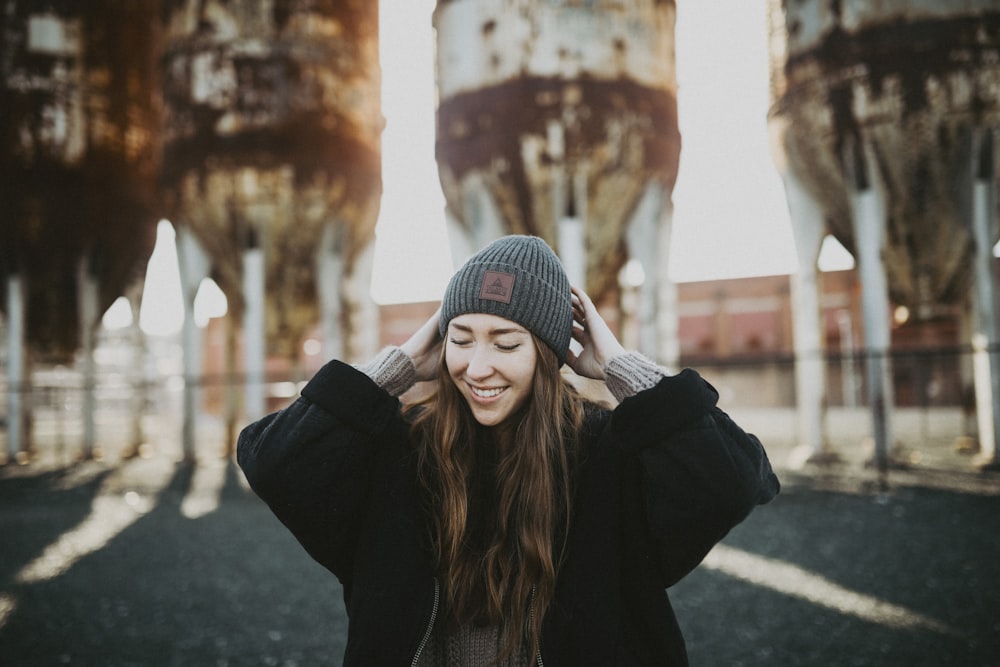 woman in black jacket and gray knit cap standing on gray concrete pavement during daytime