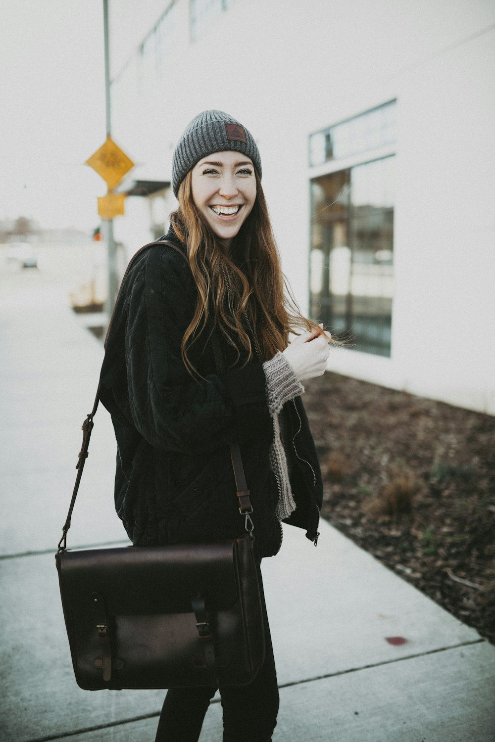 woman in black and white knit cap and black coat holding black leather sling bag