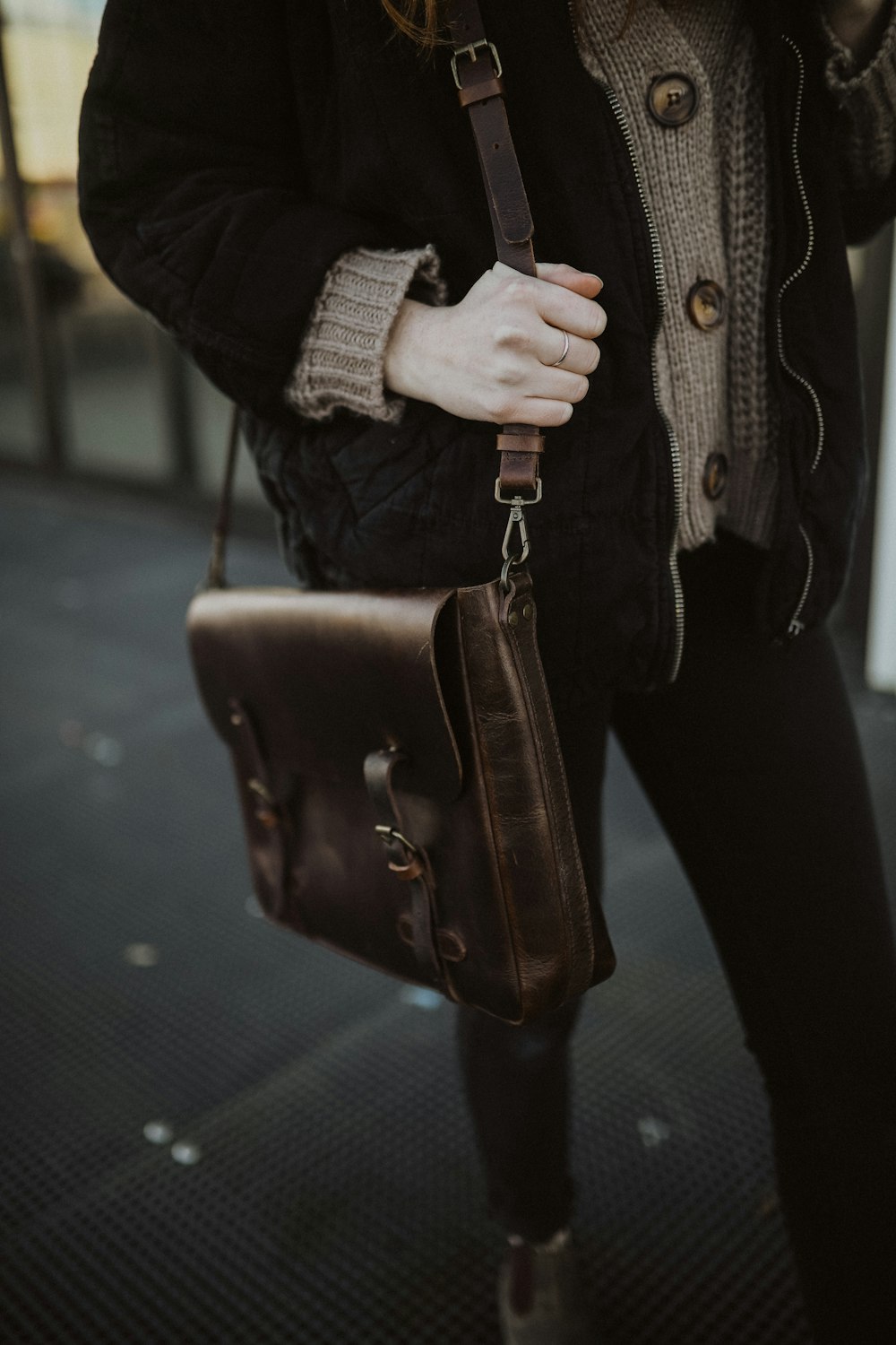 person in black jacket holding brown leather sling bag