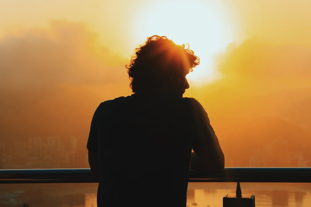 silhouette of woman standing near railings during sunset