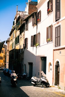 A lively street in Rome with cobblestones, scooters, and historic buildings bathed in warm sunlight.