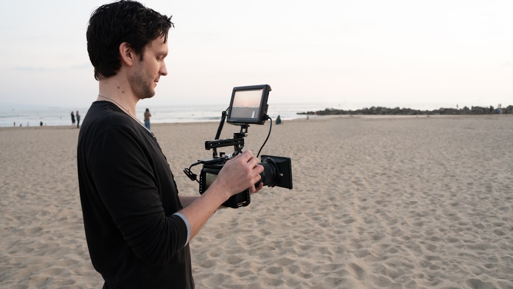man in black t-shirt holding black camera on beach during daytime