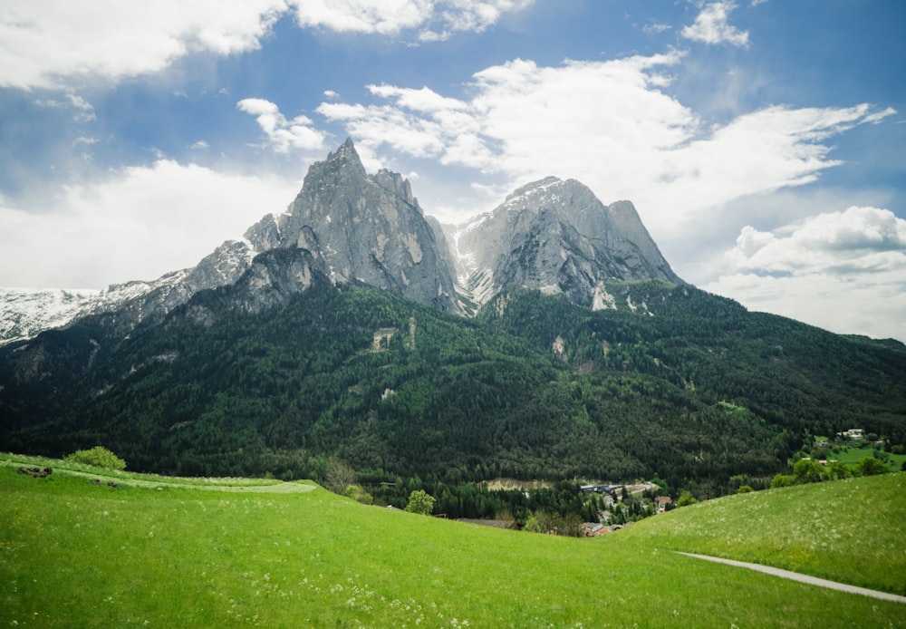 green grass field near mountain under white clouds during daytime