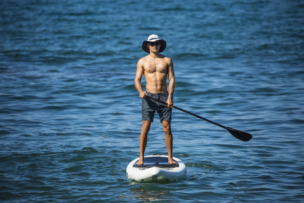 hombre en pantalones cortos azules de pie en tabla de surf blanca y negra en el cuerpo de agua durante el día