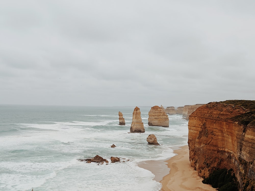 brown rock formation on sea shore under white clouds during daytime