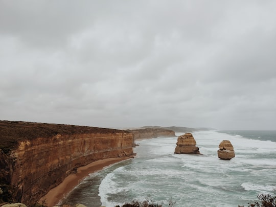 brown rock formation on sea under white clouds during daytime in Port Campbell National Park Australia