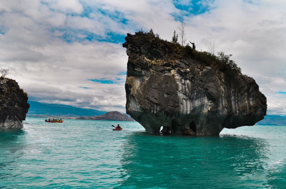 people on boat on sea near rock formation under cloudy sky during daytime