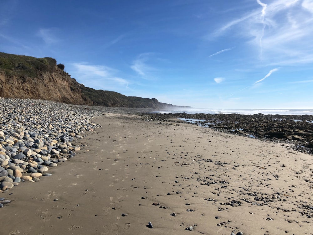 black and white stones on brown sand near body of water during daytime