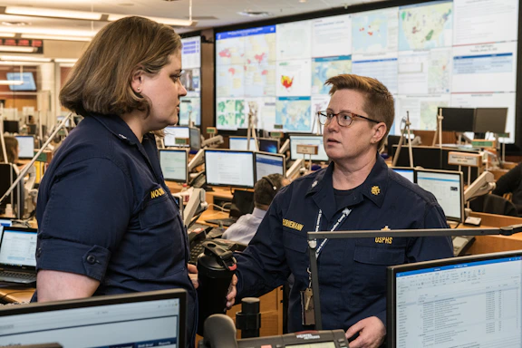 A focused professional in military uniform reviewing cybersecurity data on multiple screens in a dimly lit operations center.