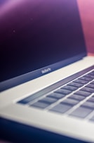 A close-up view of a modern laptop, focusing on the keyboard and partially open screen. The keyboard features a sleek design with a metallic finish, and the screen is slightly reflective, indicating a premium device.