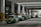 A row of green taxis are lined up under a covered structure, waiting in a designated taxi stand area. The environment has industrial features with pillars and signage in both English and another language. The concrete surface and overhead fluorescent lighting contribute to a utilitarian atmosphere.