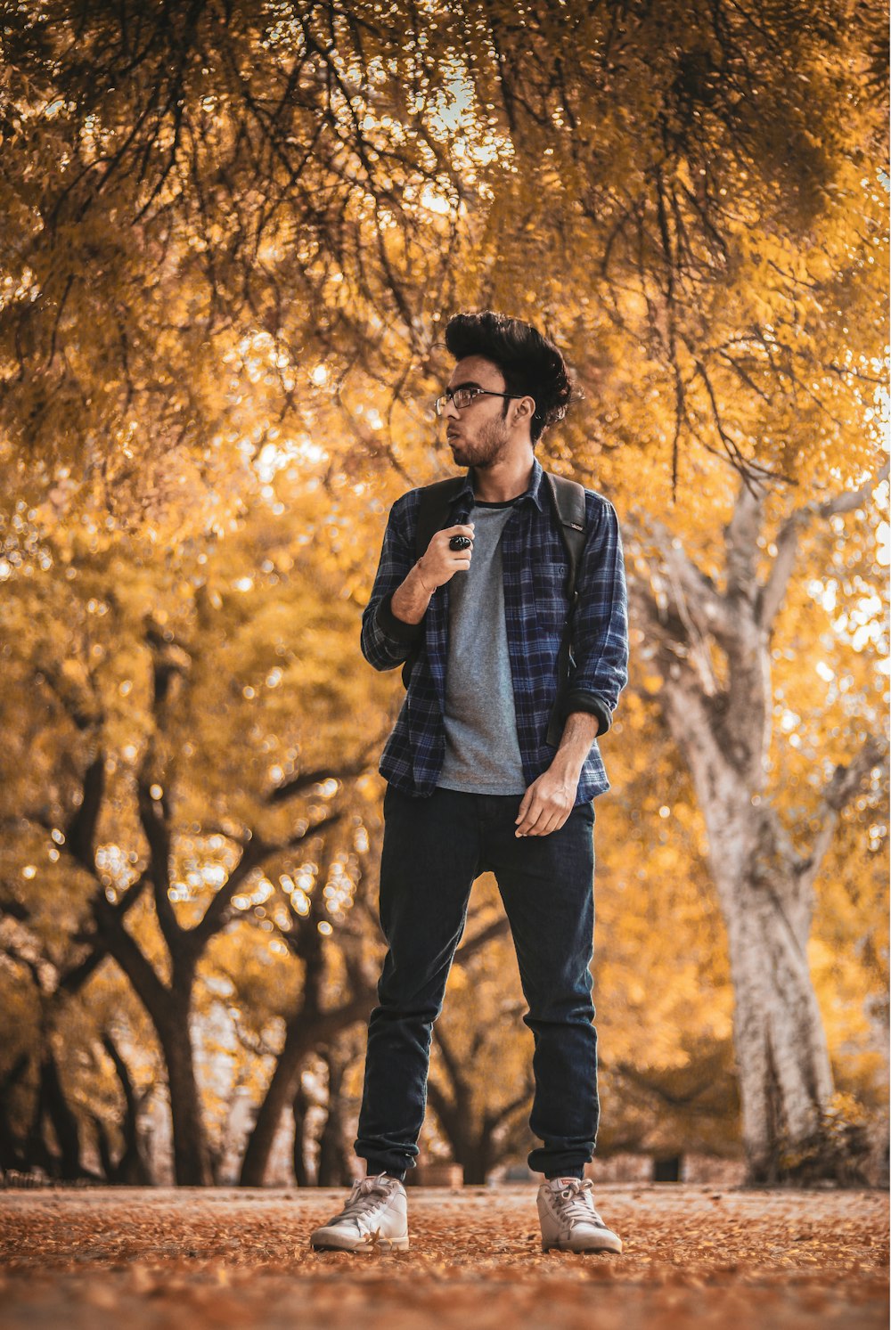 man in black and gray plaid dress shirt and black pants standing near brown trees during