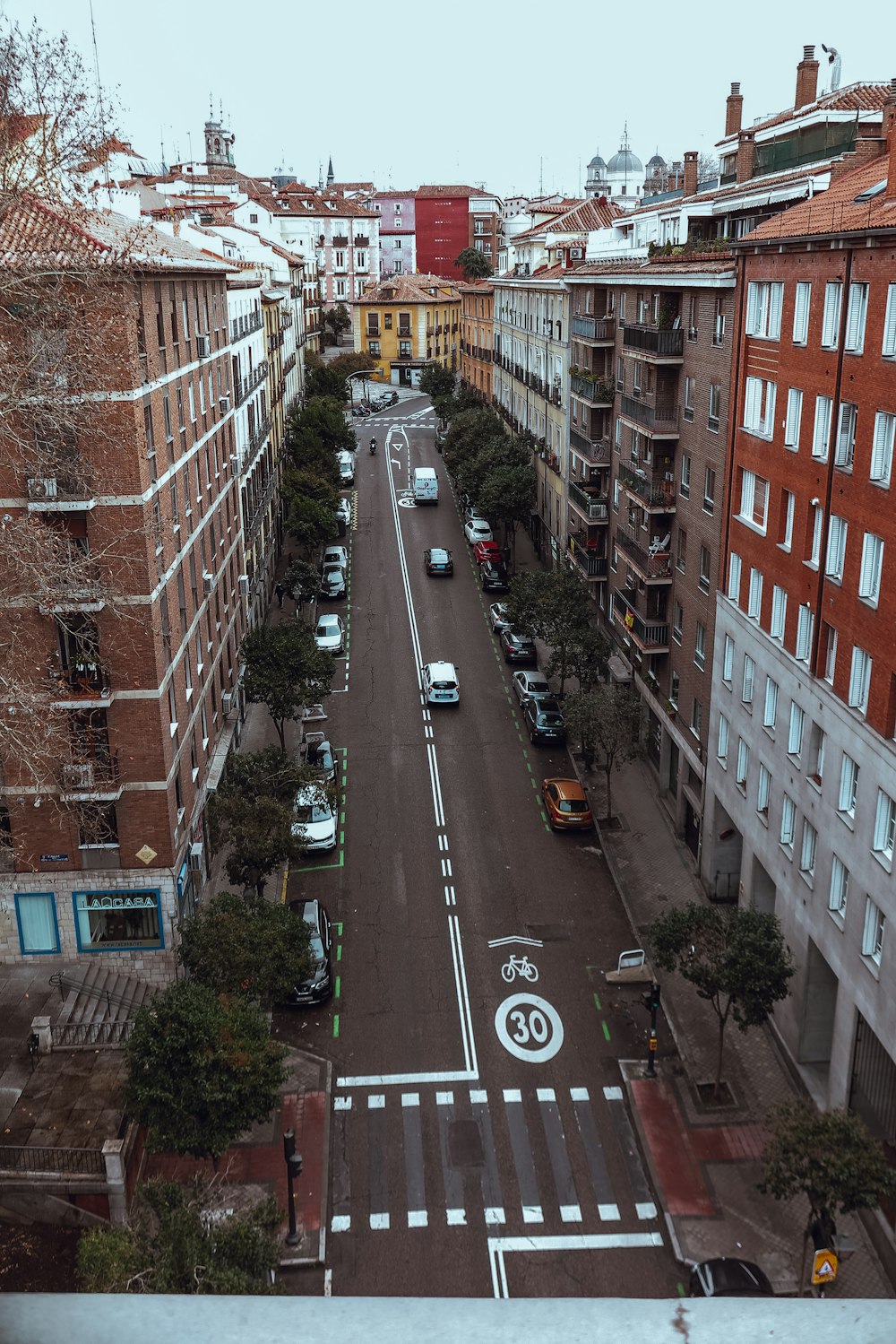 cars parked on the side of the road in between of brown brick buildings during daytime