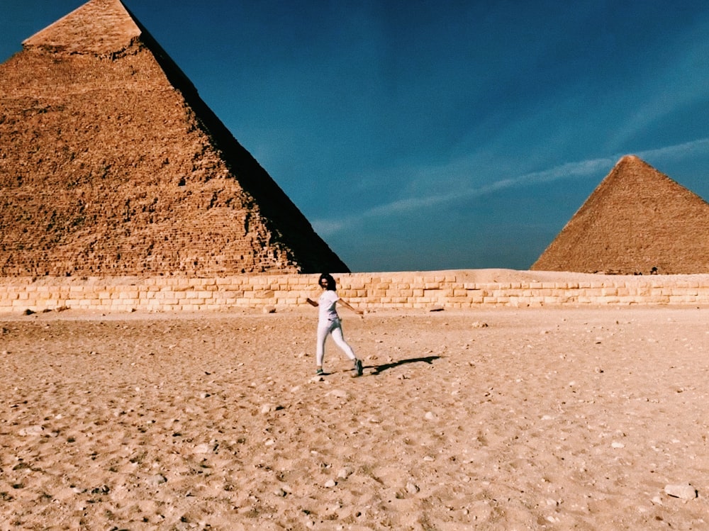 man in white shirt and gray pants walking on brown sand during daytime