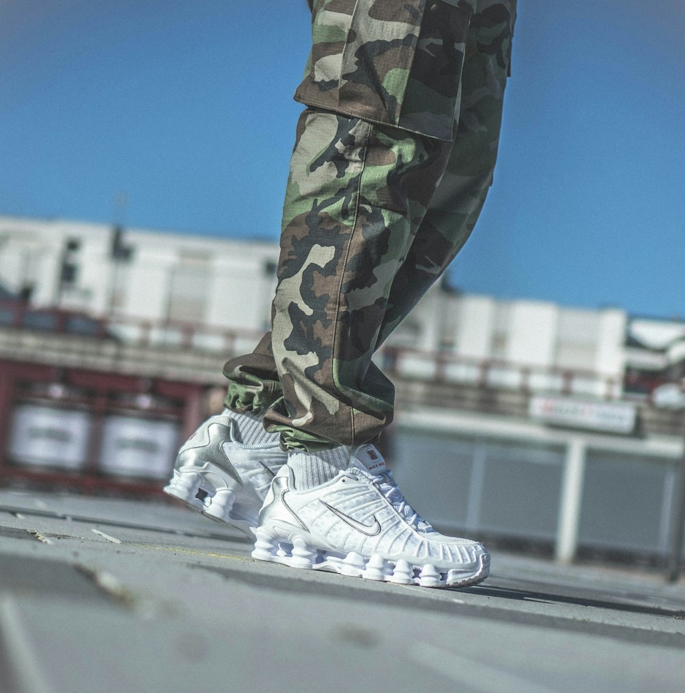 person in green and brown camouflage pants and white nike sneakers