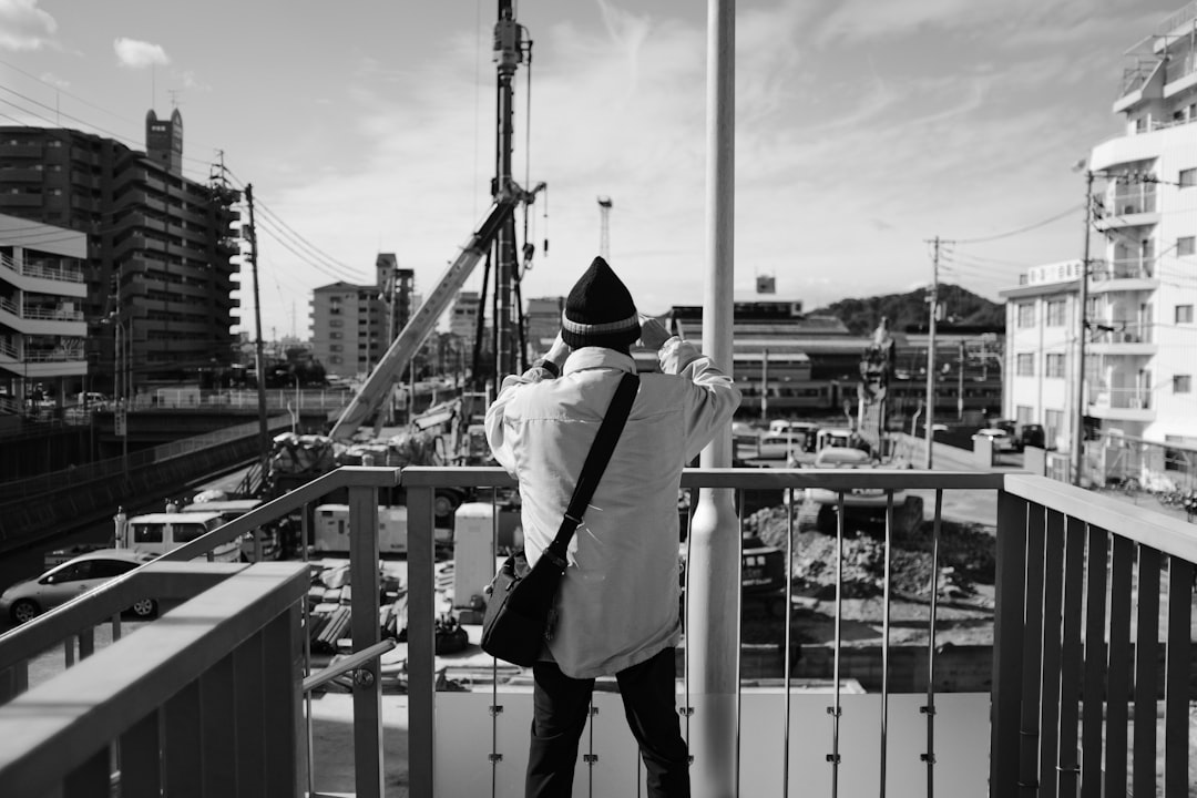 grayscale photo of man in white dress shirt and black pants standing on bridge