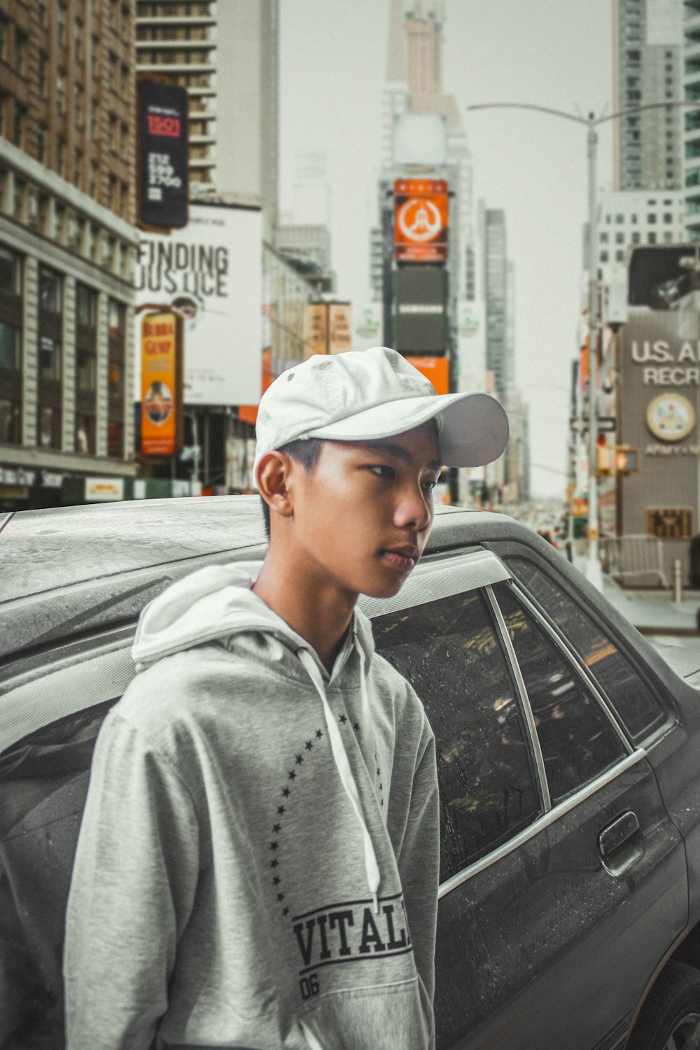 man in gray hoodie standing beside black car during daytime