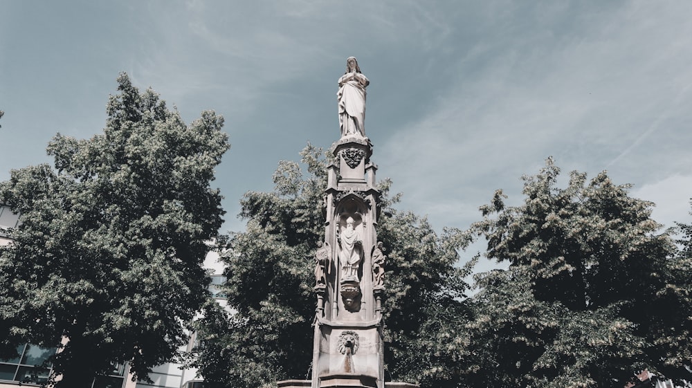 Statua di cemento marrone e bianco vicino agli alberi verdi sotto il cielo blu durante il giorno