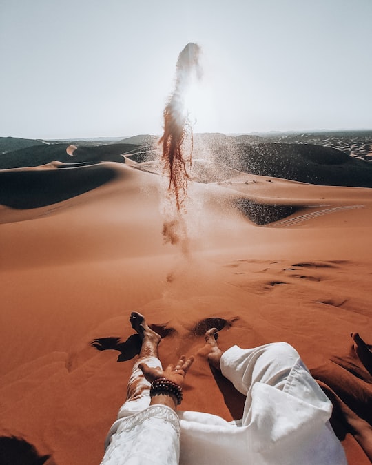 person in white pants sitting on brown sand during daytime in Merzouga Morocco