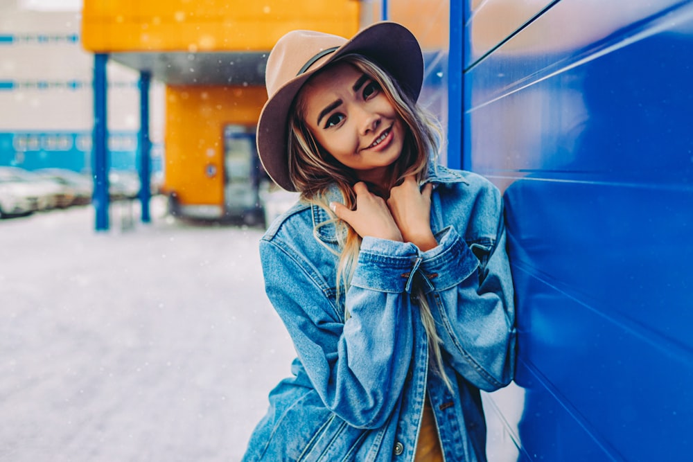 woman in blue denim jacket and black hat standing near blue metal fence during daytime
