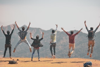 group of people jumping on brown sand during daytime