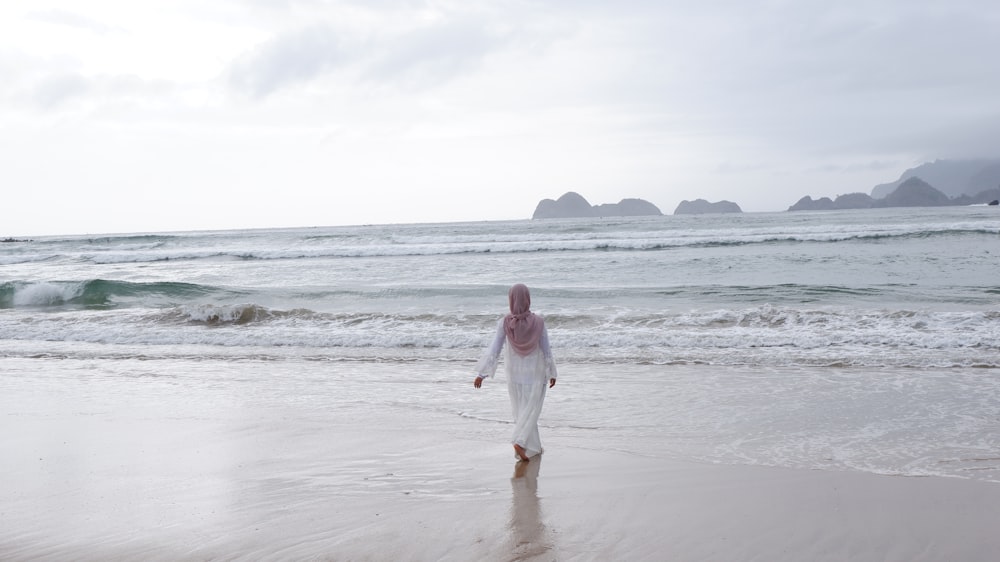 woman in white long sleeve shirt walking on beach during daytime