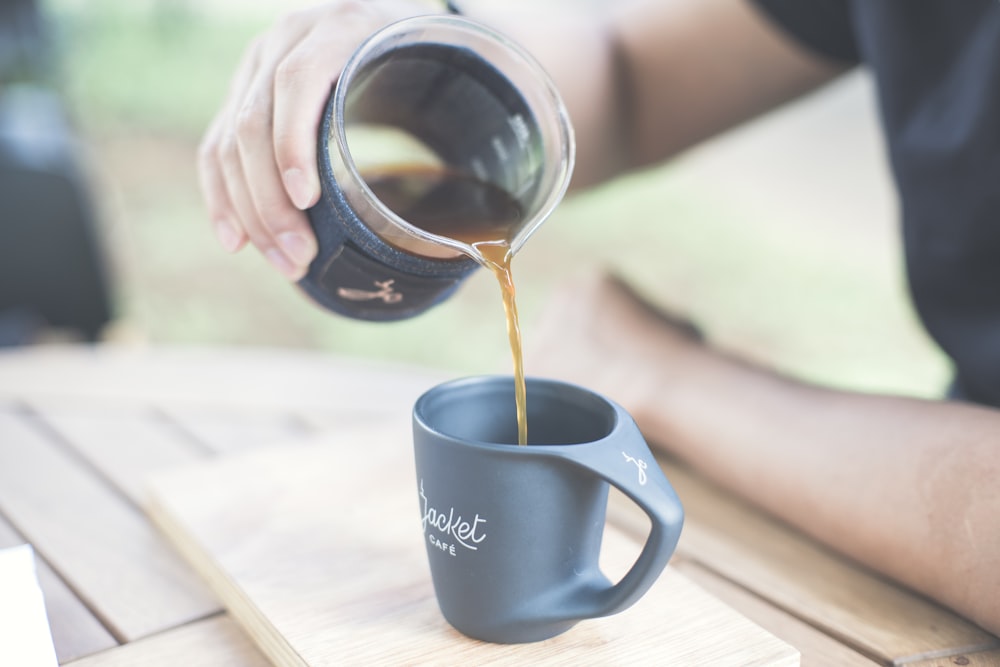 person holding black ceramic mug with brown liquid