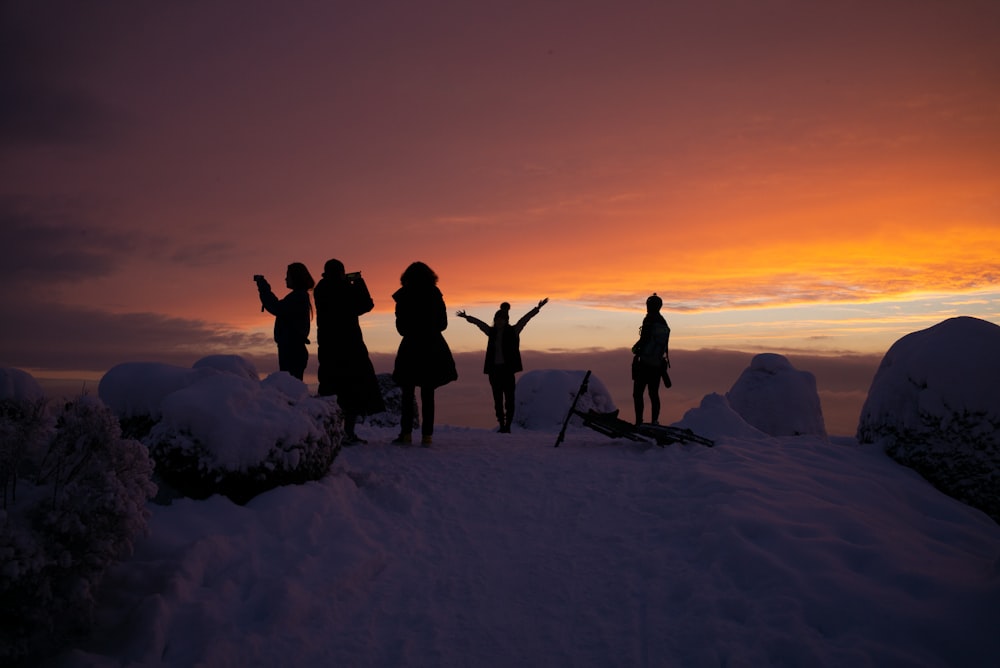 silhouette di persone su terreno coperto di neve durante il tramonto