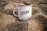 A white mug with the text 'IZHAK Creative Intelligence' printed on it is placed in a setting of sand. The mug is positioned upright, surrounded by grainy sand, and it appears to be a calm and serene environment.