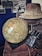 A vintage scene featuring a large globe on a stack of old leather suitcases. There is an explorer hat placed on top, alongside a pair of binoculars in a worn leather case. Black and white photographs of landscapes are displayed on the wall in the background.
