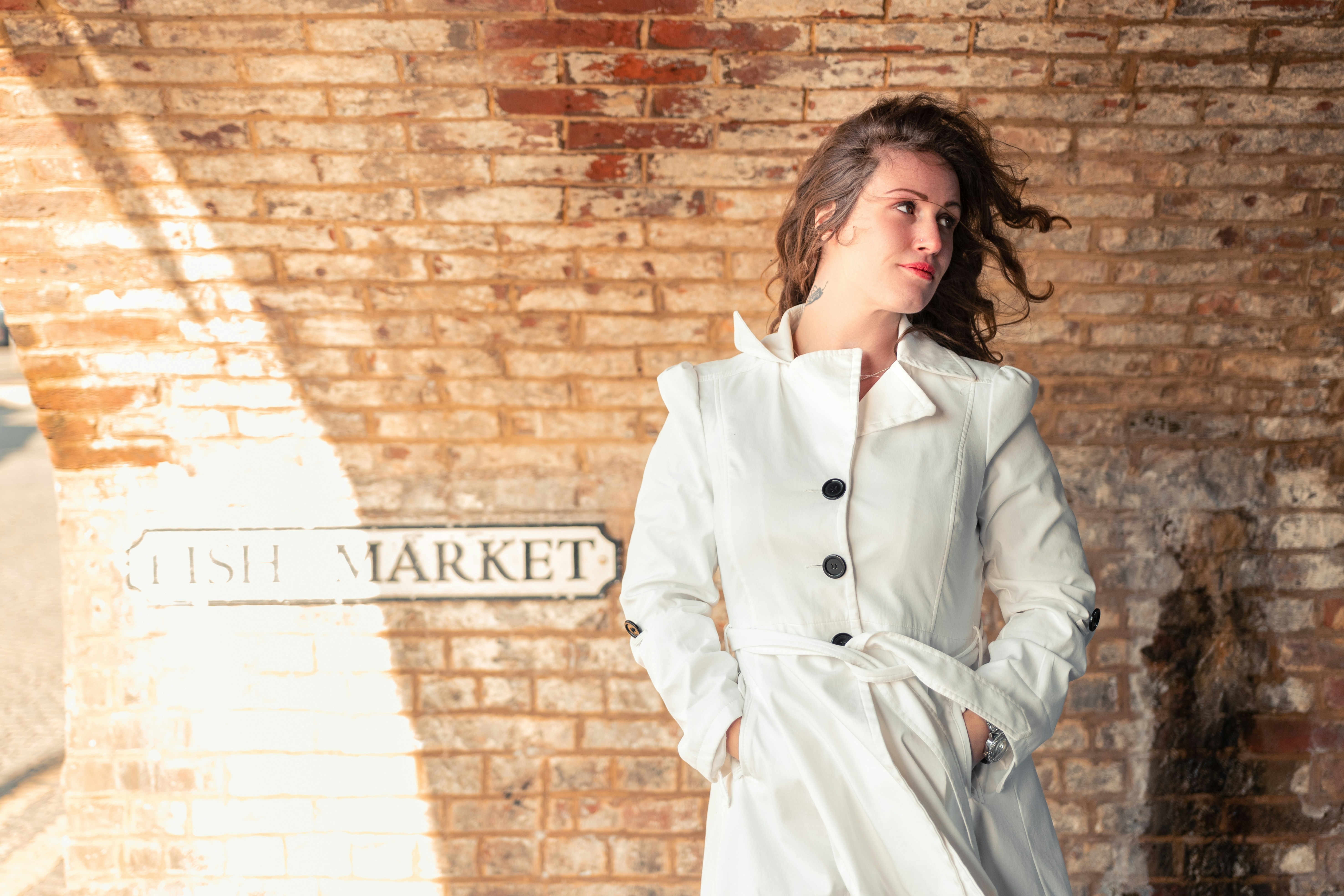 woman in white coat standing beside brick wall