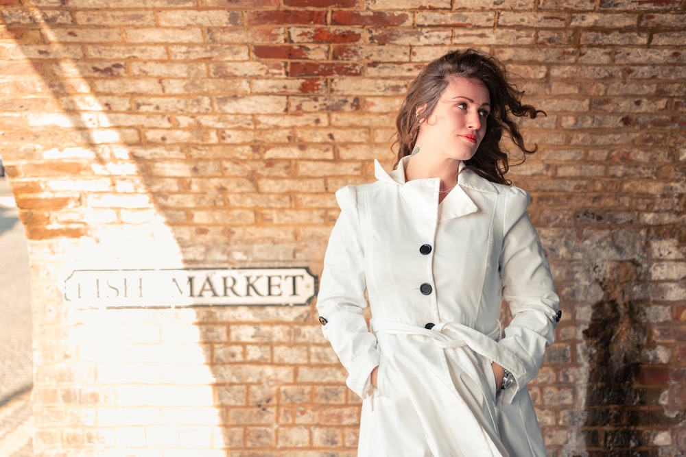 woman in white coat standing beside brick wall
