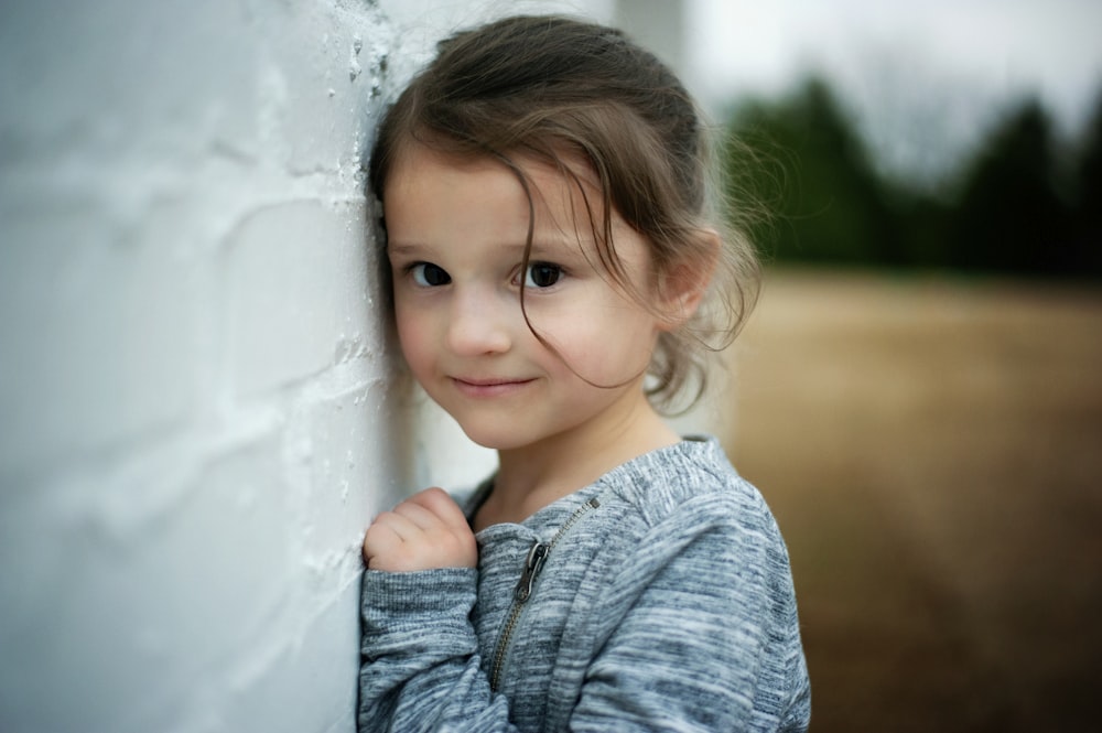 girl in blue denim jacket leaning on white wall