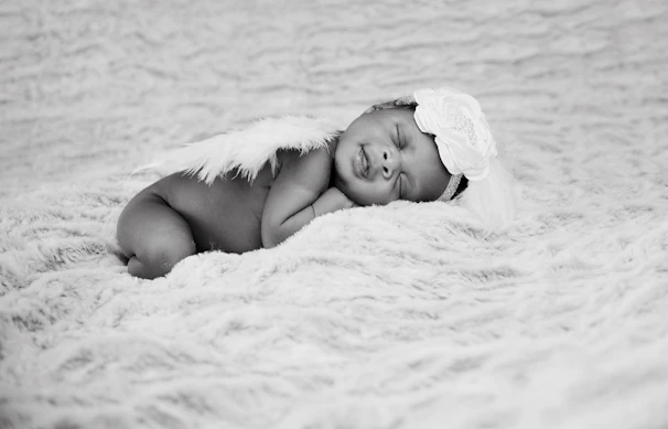 Softly wrapped newborn peacefully sleeping in a pastel pink blanket with delicate floral headband.