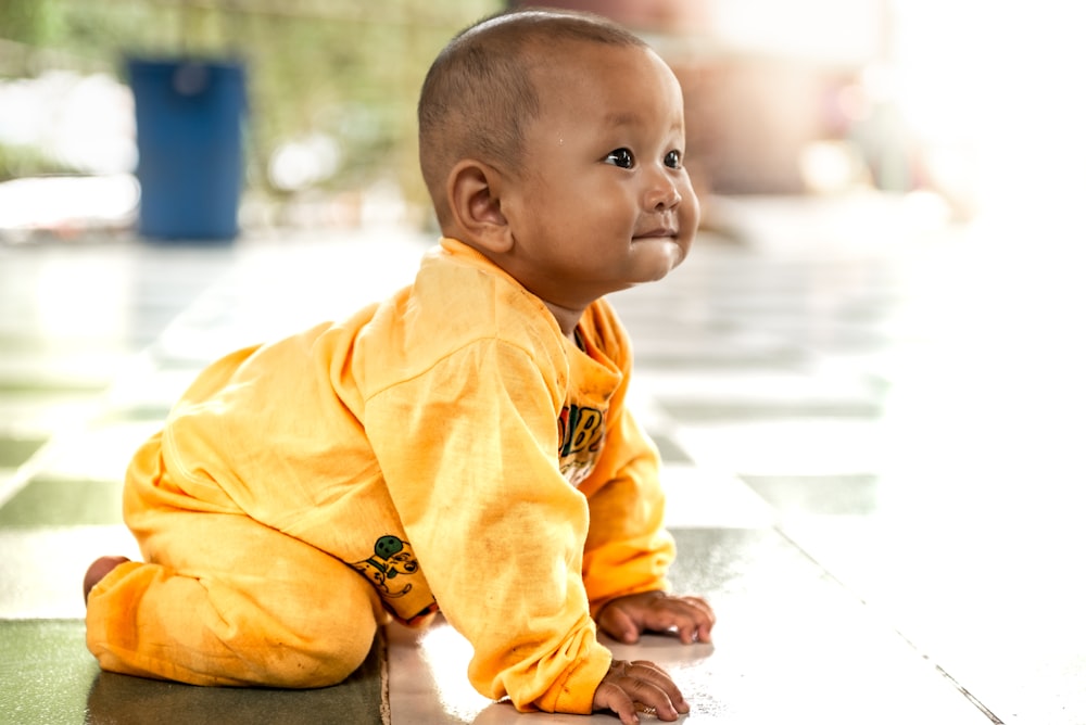 baby in yellow onesie lying on floor