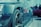 A close-up of a car wheel and part of the side body, showcasing the intricate details of the tire tread and alloy rim. The scene has a blurred background with shapes that suggest other cars and people, indicating a gathering or car show environment.