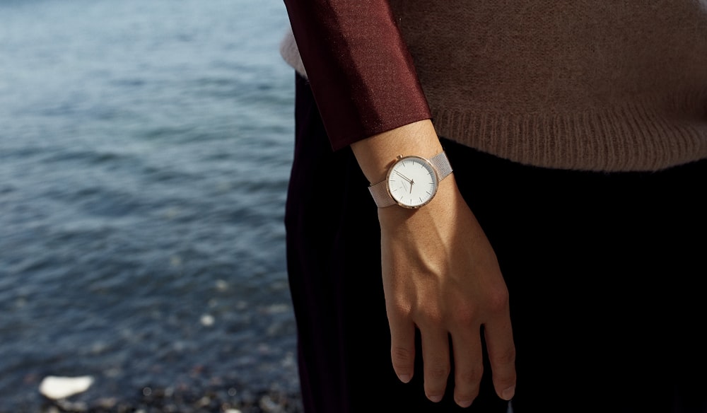 person in brown sweater and black pants wearing white analog watch
