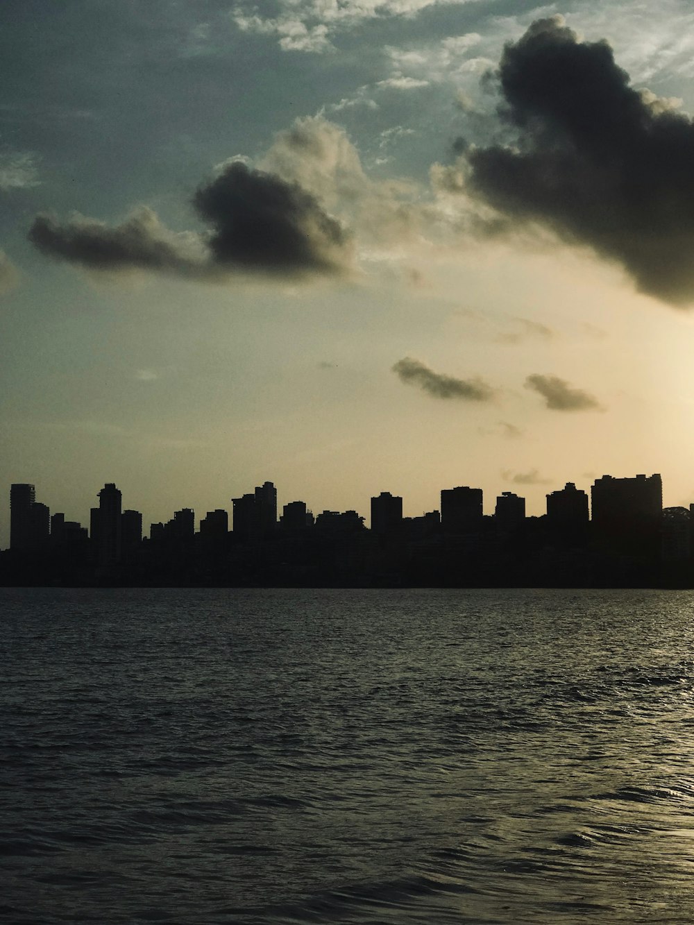 silhouette of city buildings near body of water during sunset