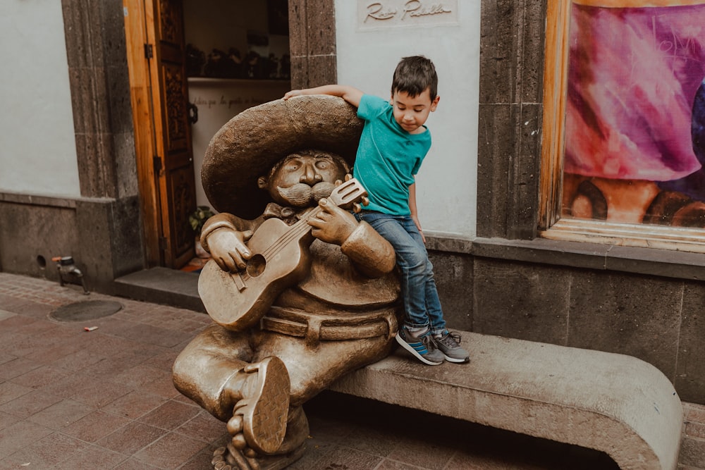 boy in blue long sleeve shirt and blue denim jeans sitting on brown concrete statue