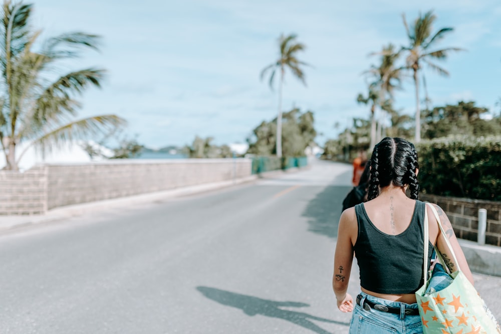 woman in black tank top and blue denim jeans standing on road during daytime