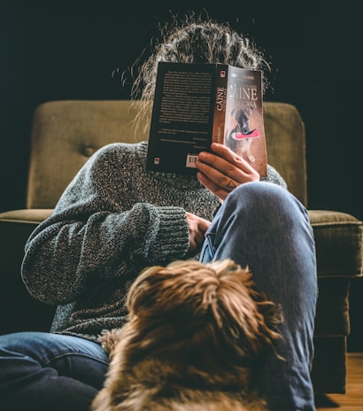 person in blue denim jeans sitting on brown sofa chair reading book