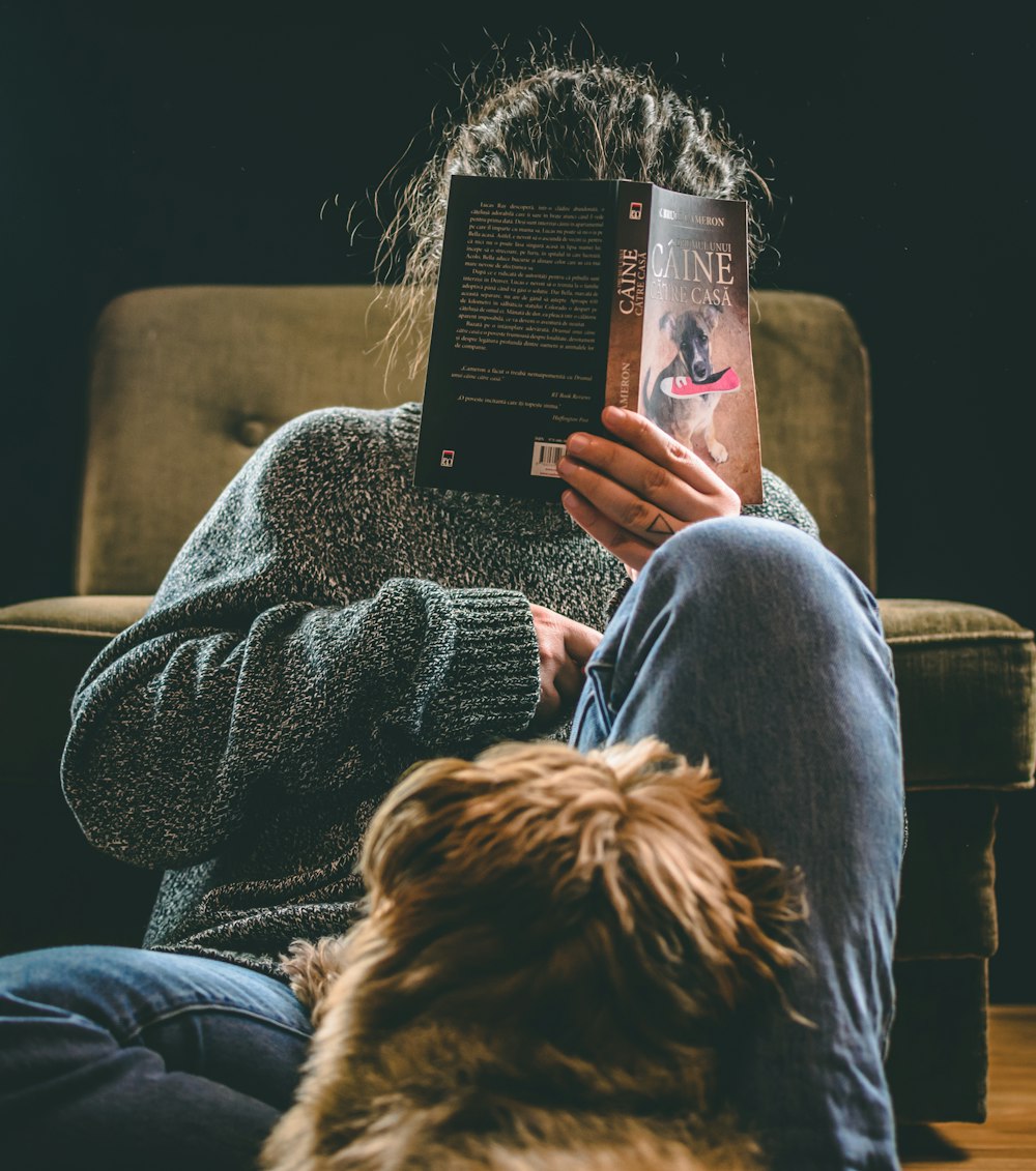 pessoa em jeans azuis sentados na cadeira marrom do sofá lendo o livro