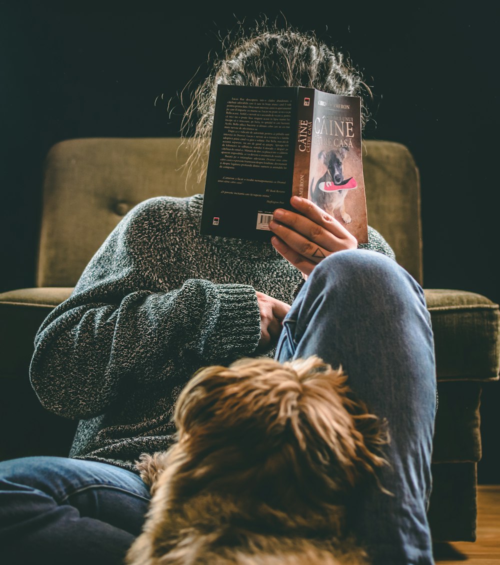 person in blue denim jeans sitting on brown sofa chair reading book