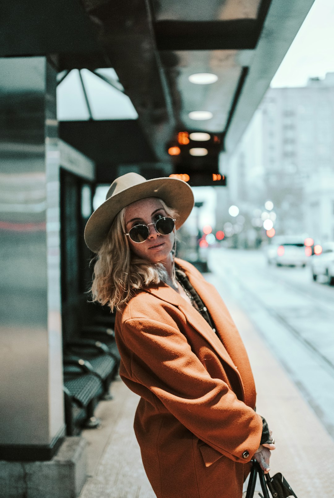 woman in brown coat and black hat standing on sidewalk during daytime