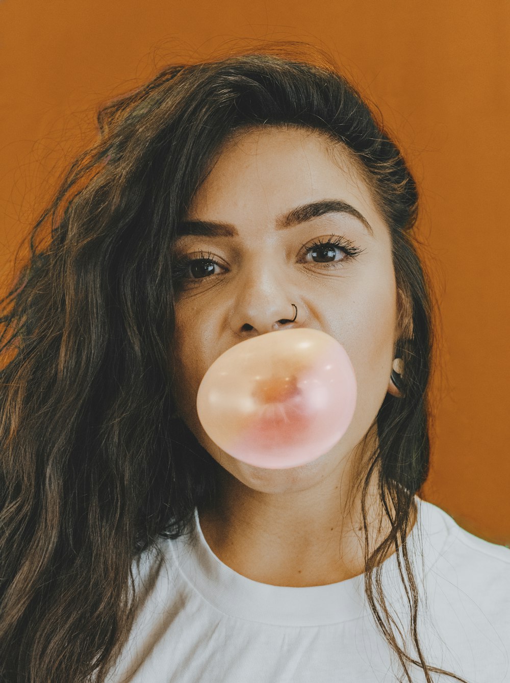 femme en chemise blanche à col rond soufflant une bulle