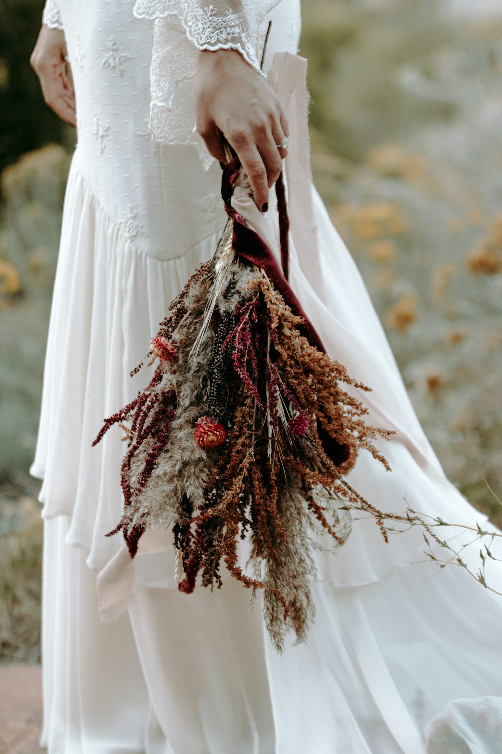 woman in white dress holding red and brown bouquet