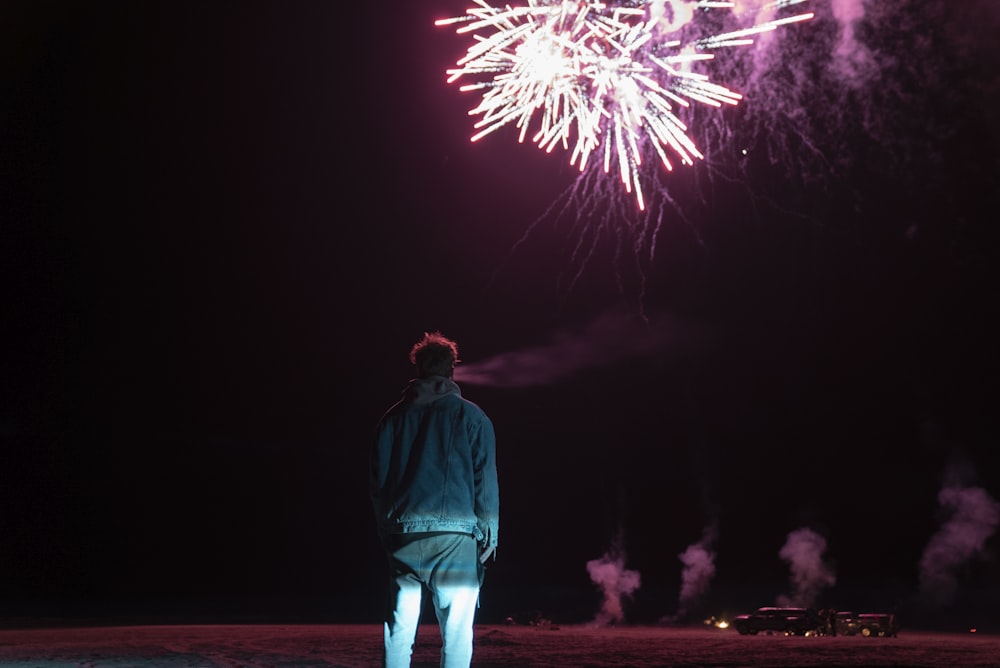man in green jacket standing on brown sand with fireworks display during nighttime