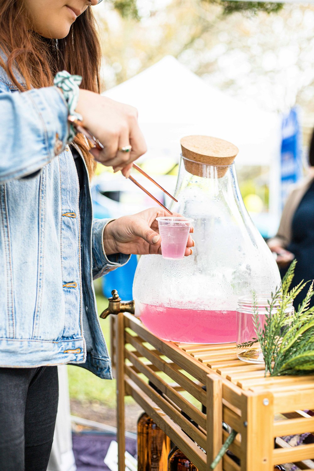 person in blue denim jacket holding clear glass pitcher with red liquid